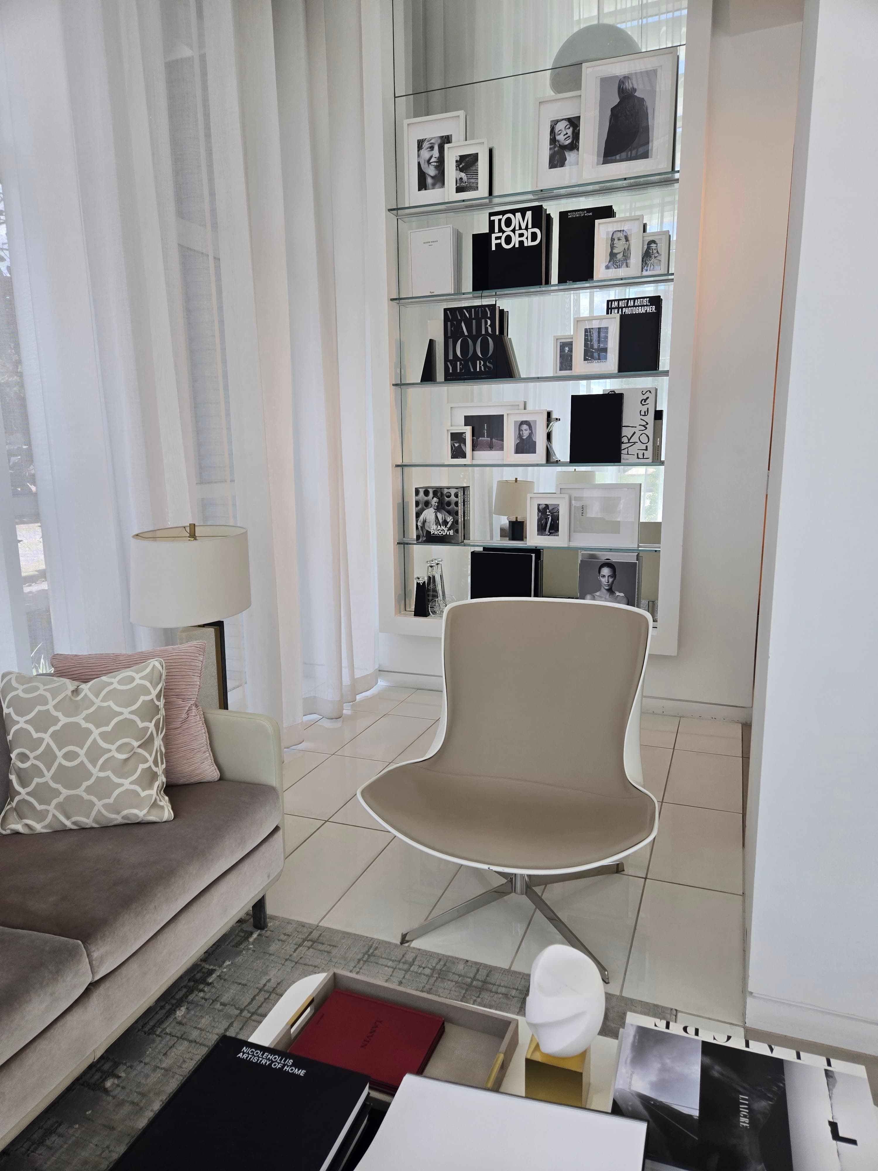 Mirror Mirror waiting area with upholstered seating, sheer curtains, and glass shelves of art books and framed photographs.